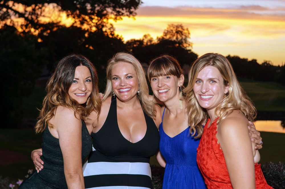 Group of friends enjoying sunset outdoors wearing vibrant dresses in blue, white and coral colors.
