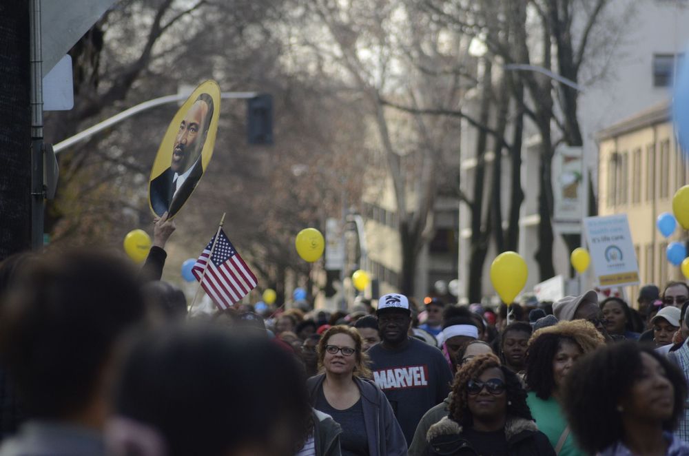 Crowd of protesters marching through a city street with signs and American flags during a demonstration.