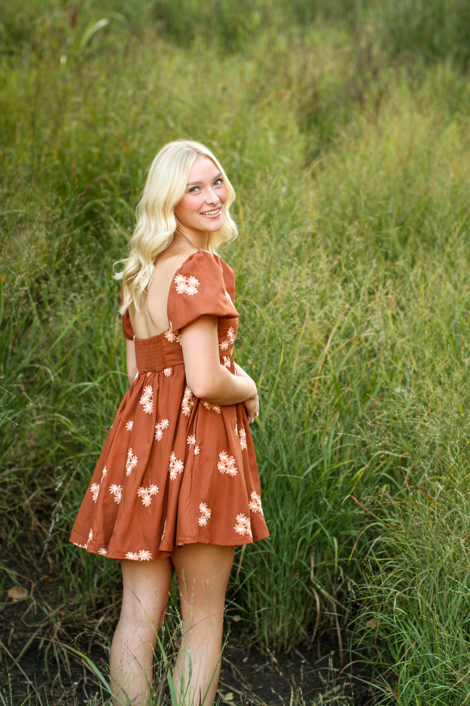 A young woman looks over her shoulder as she frolics through a tall field of green grasses during her Kansas City senior photos.