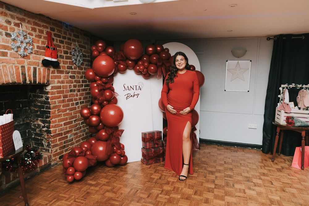 Red balloon arch decorates a brick wall corner at a holiday party with festive decor and parquet flooring.