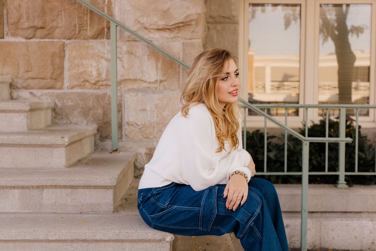 Person in white blouse and blue jeans sits casually on stone steps in warm sunlight.