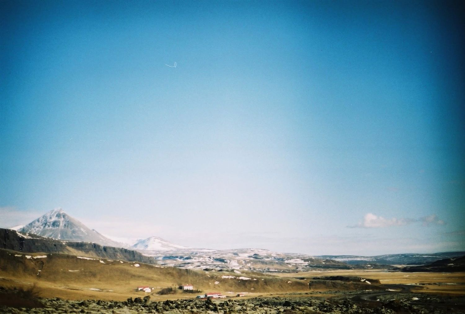 A vast mountain landscape with rolling hills and rocky terrain under a clear blue sky with vignette edges.