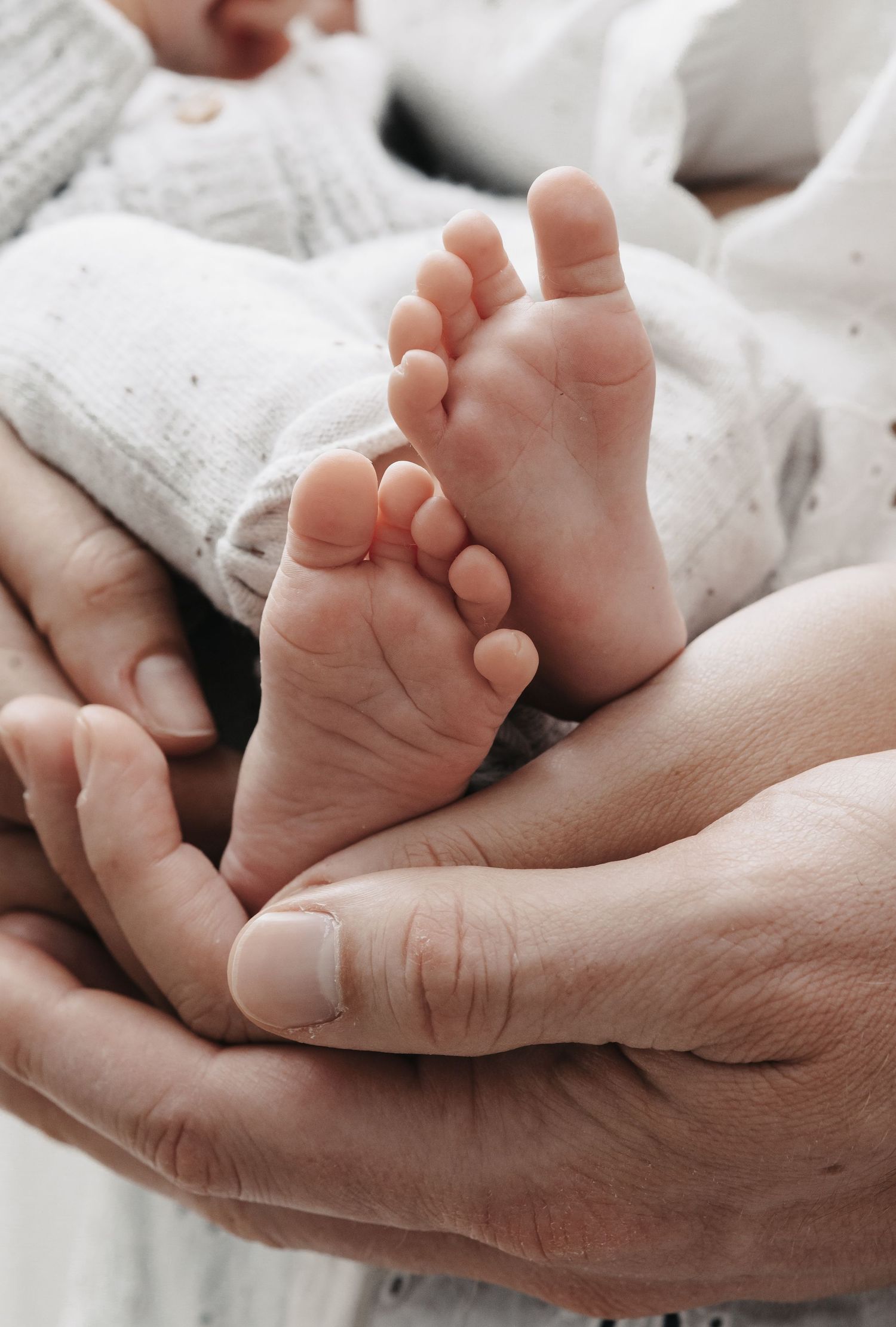 Gentle hands cradle a newborn baby's head with soft brown hair against light-colored fabric in an intimate moment.