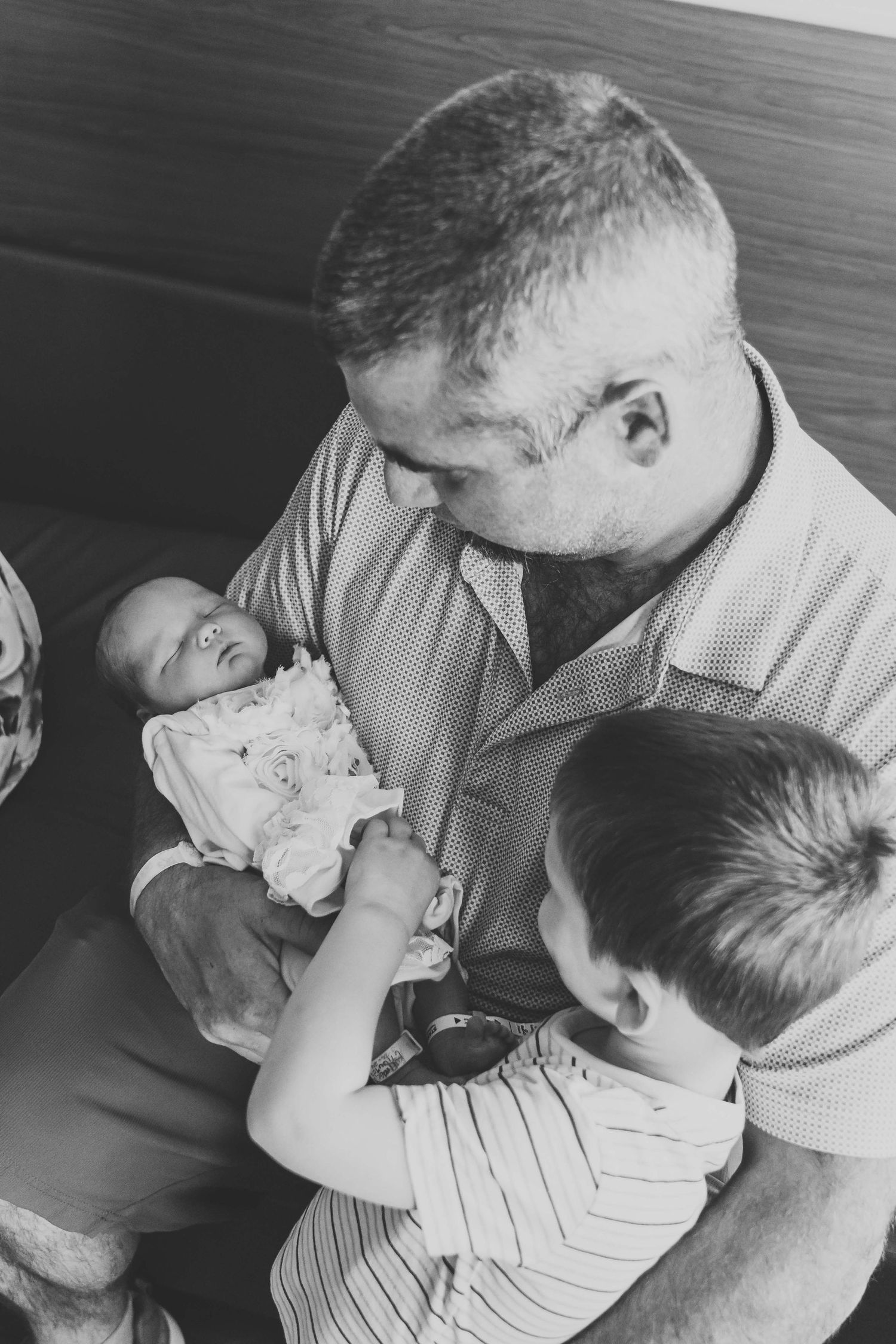 Black and white photograph of a person in striped shirt holding a baby while a young child looks on.