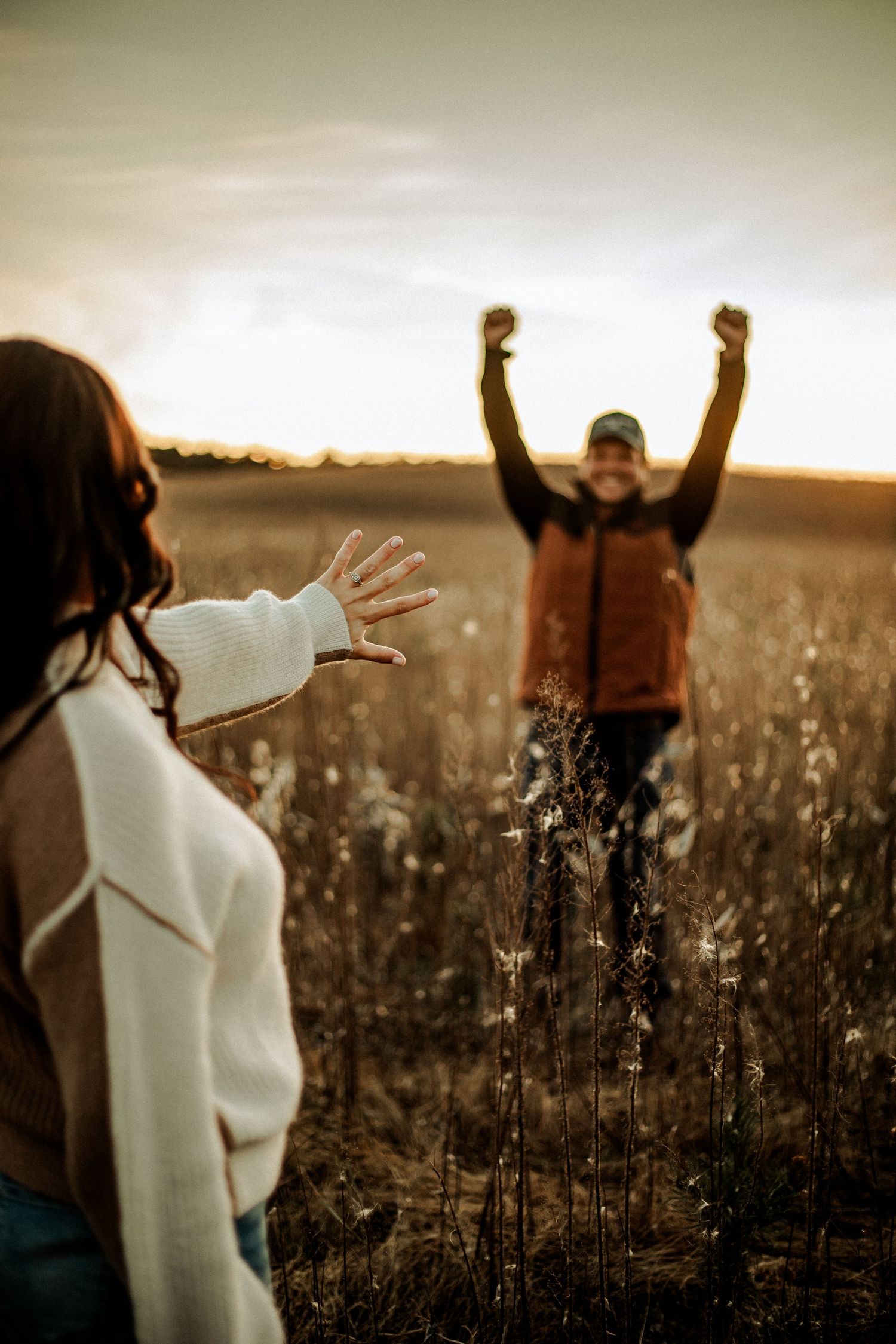 Silhouette of two people in a golden field during sunset with one person raising their arms.