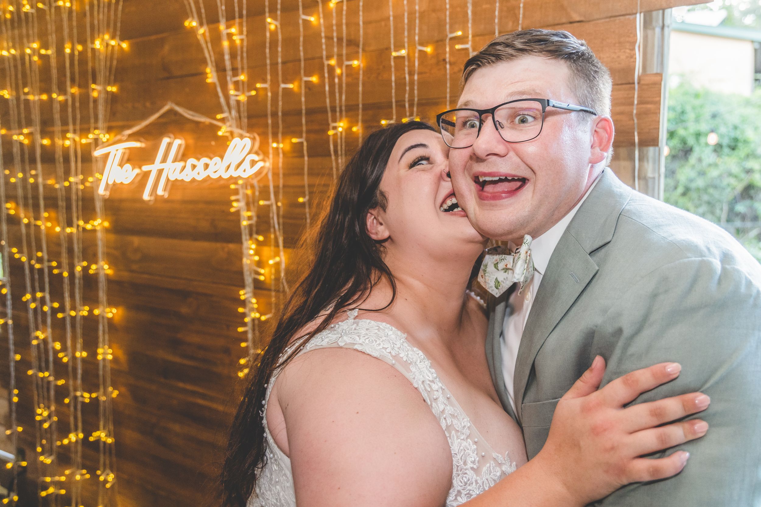 Joyful wedding moment captured against glowing neon lights and fairy light backdrop.