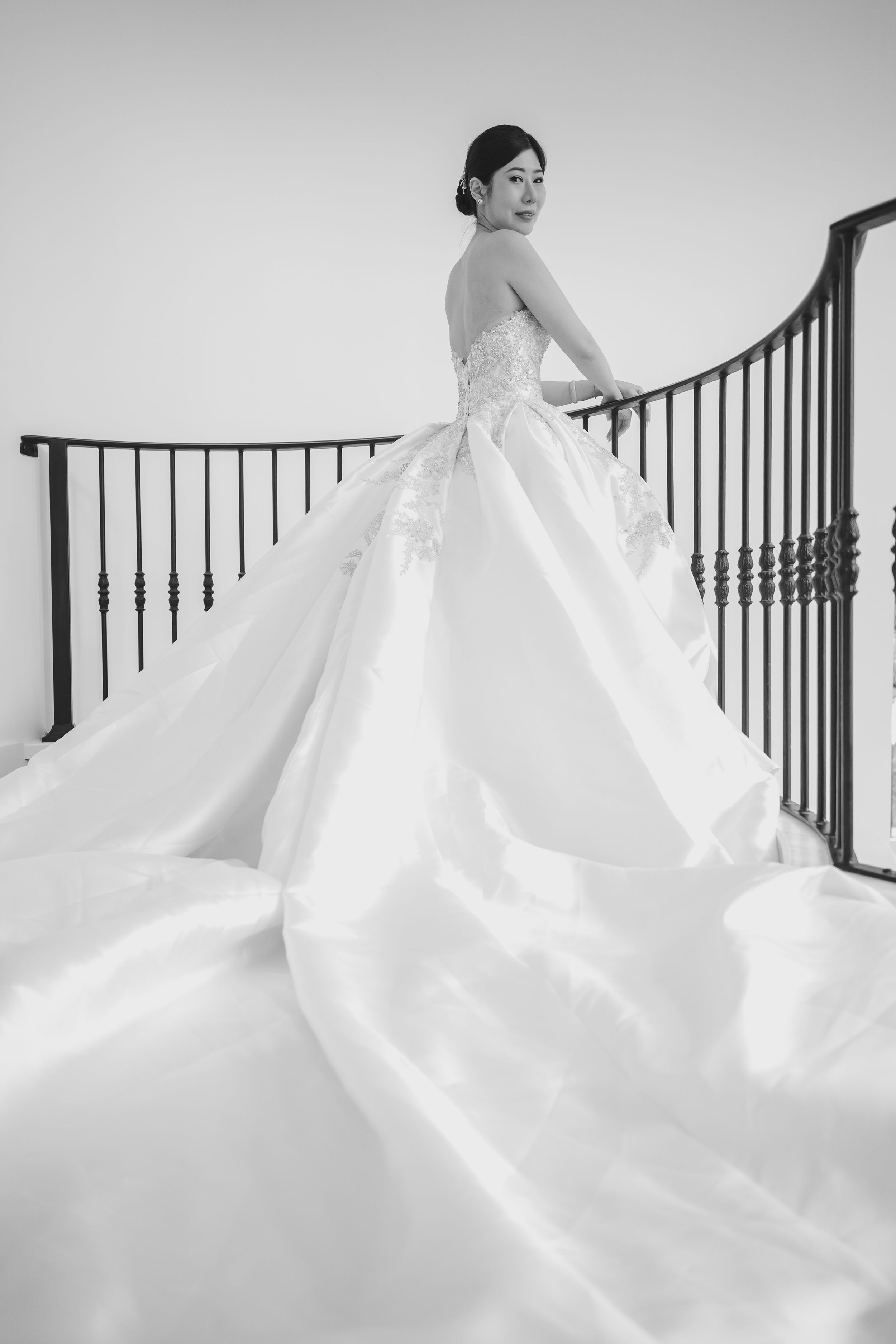 A stunning white wedding gown with a dramatic flowing train shown against a curved staircase railing.