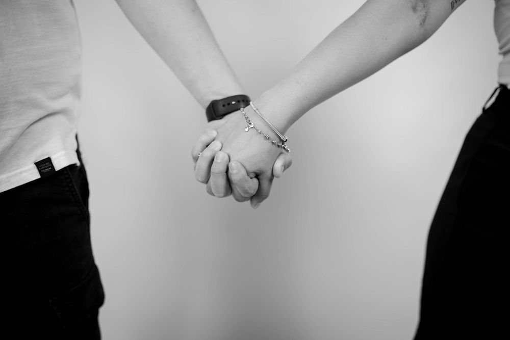 A black and white close-up of two people holding hands intimately.