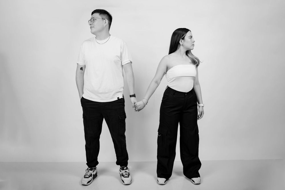 A minimalist black and white portrait of a couple standing back to back while holding hands.