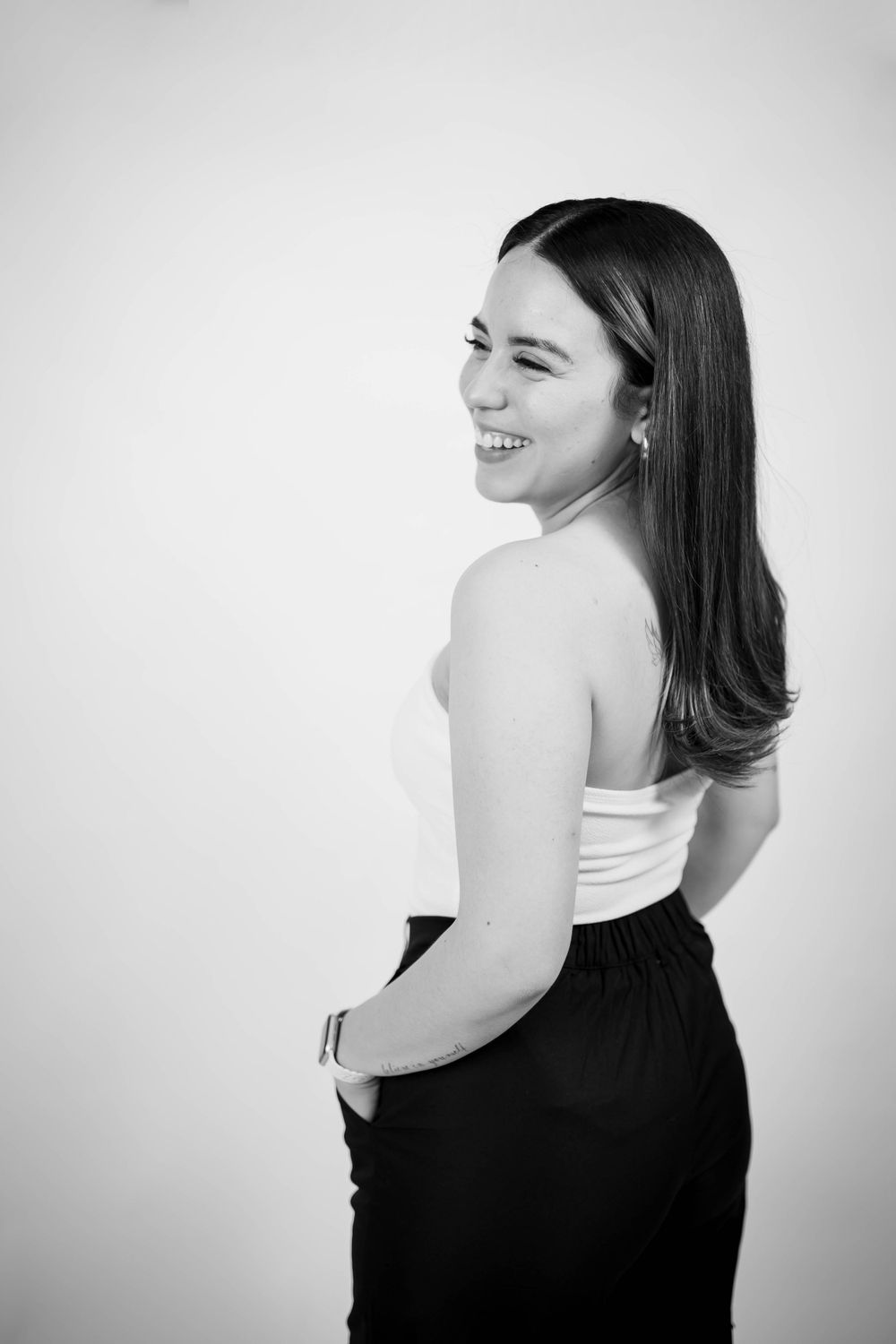 Black and white portrait of someone in a white top and dark pants smiling over their shoulder.