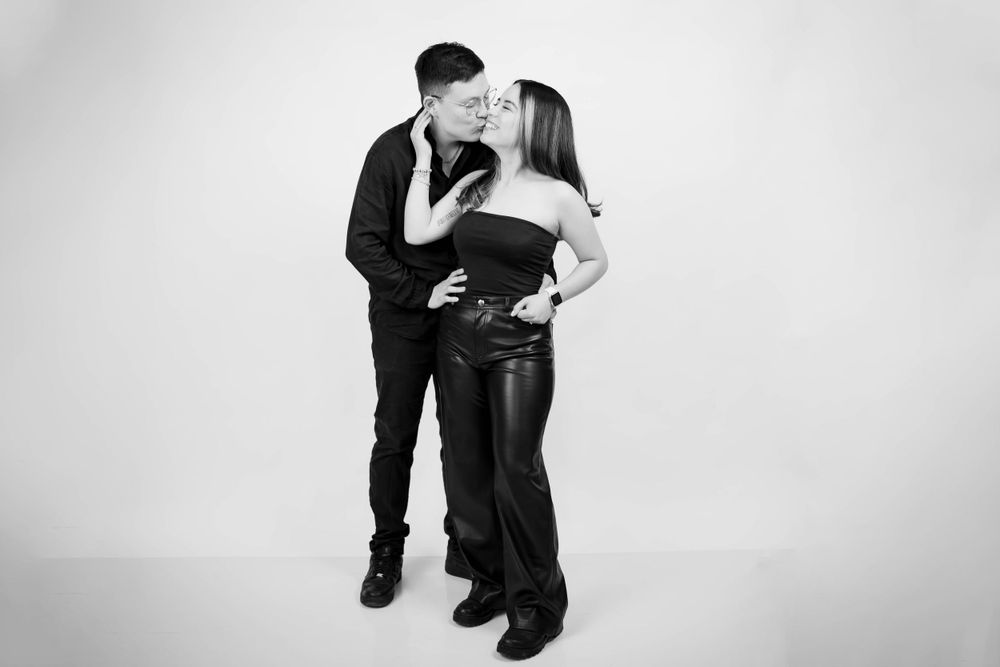 A romantic black and white portrait of a couple embracing in casual attire against a plain background.