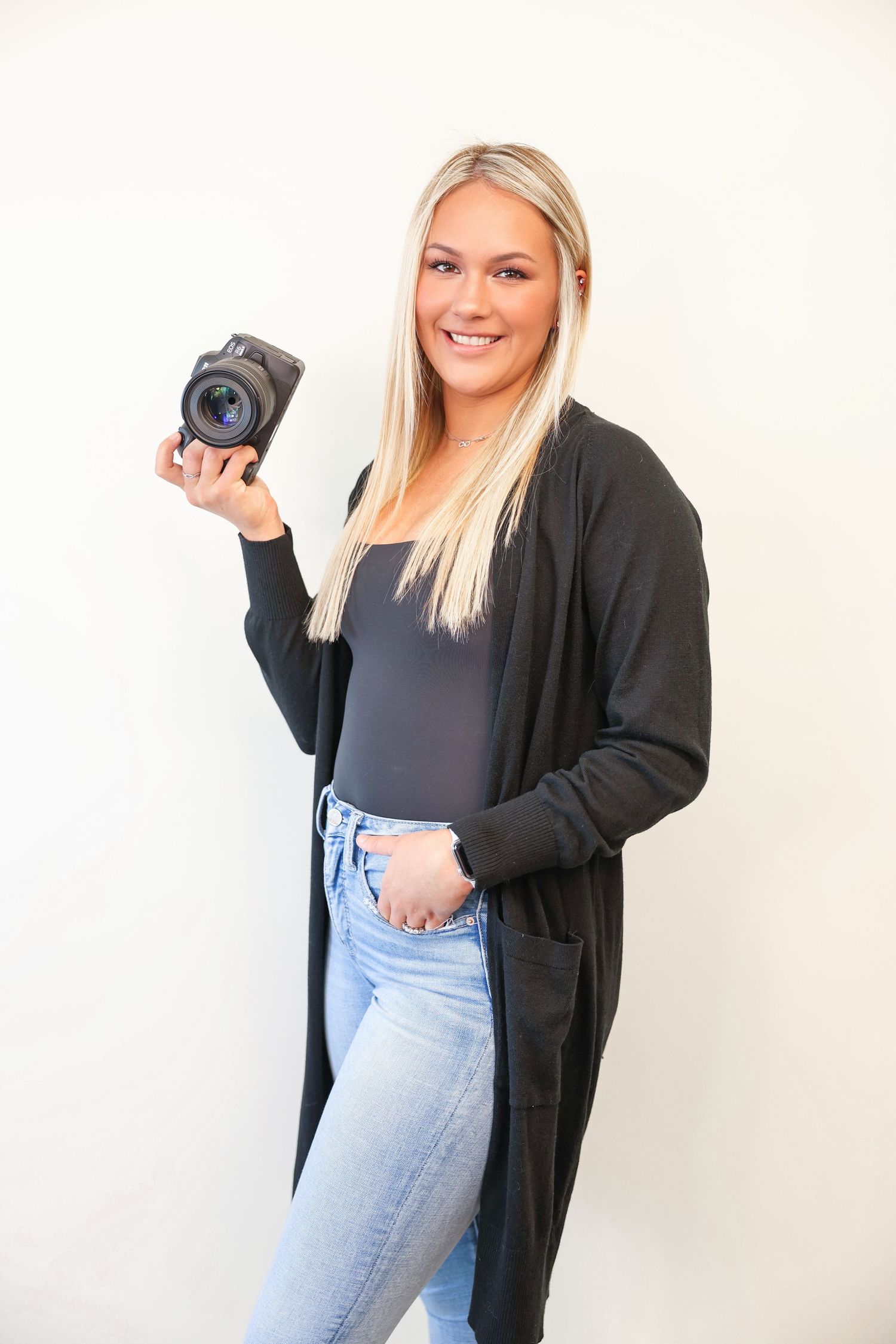 Professional photographer in casual attire holding a DSLR camera against white background.