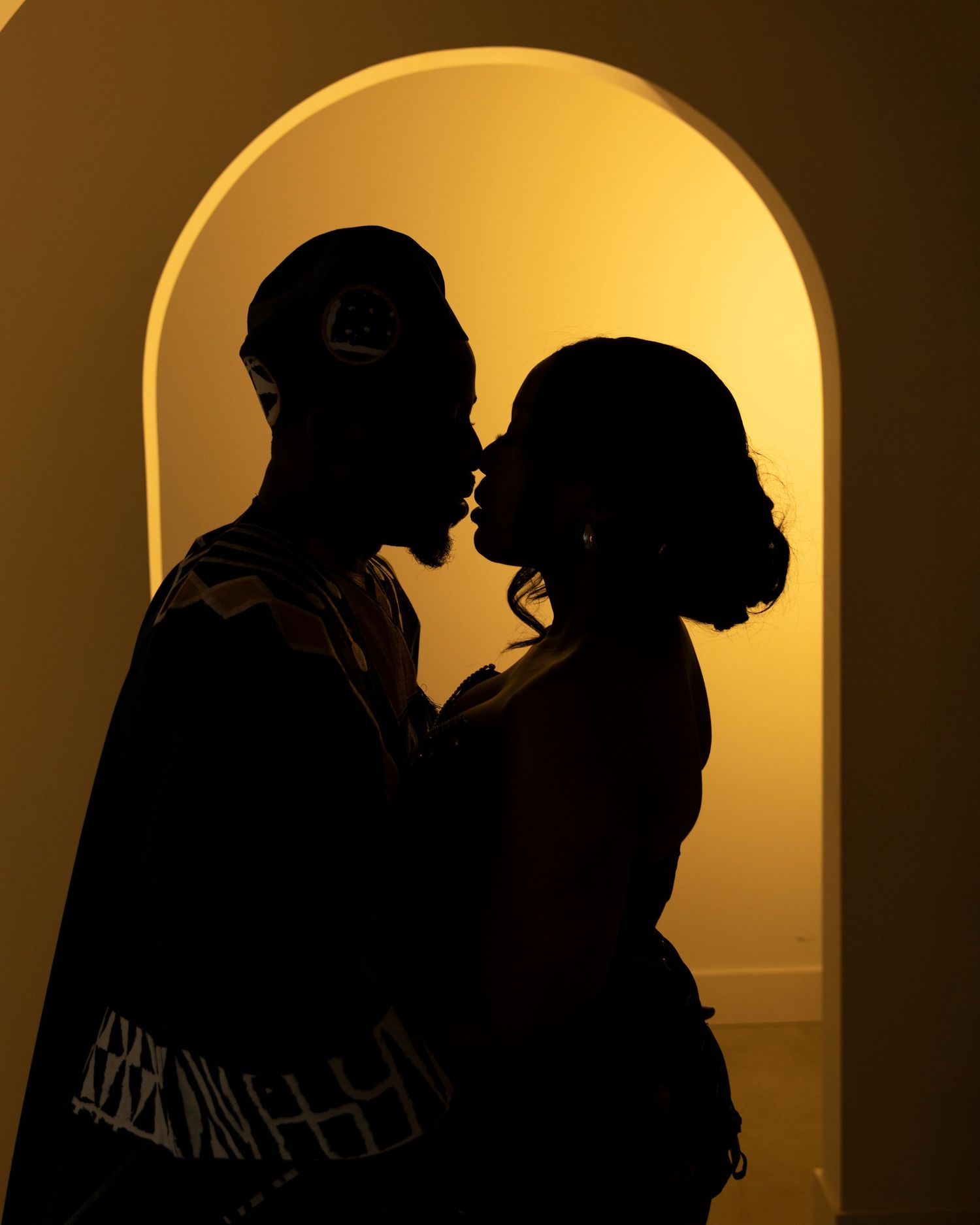 Silhouette of a couple in a romantic embrace against a golden backlit archway at sunset.