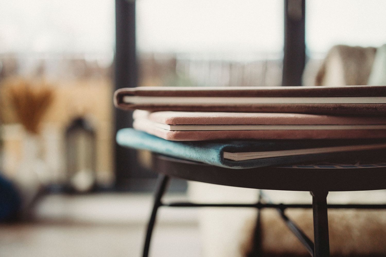 Stack of notebooks or journals with leather covers resting on a dark metal table with blurred background.