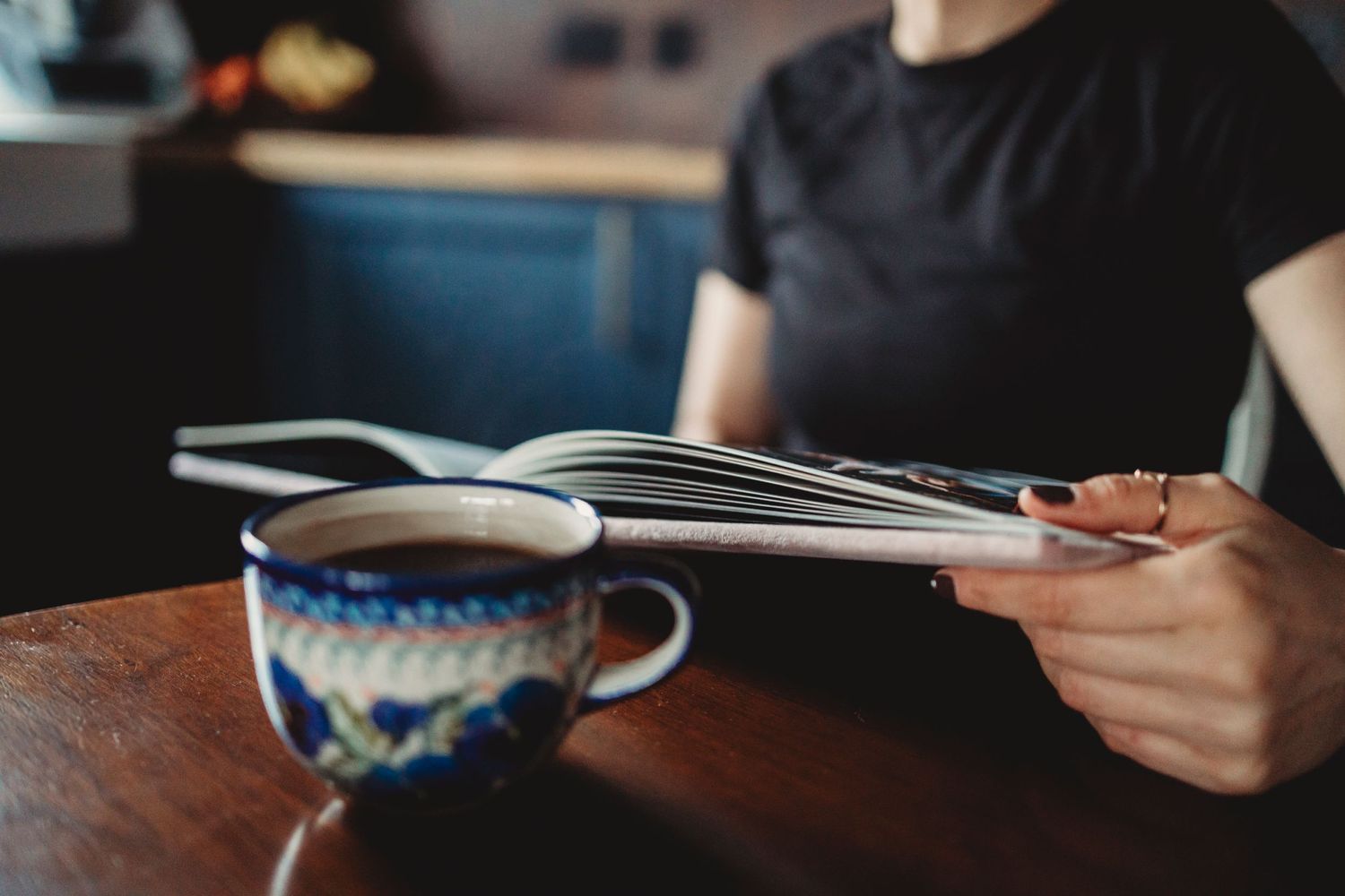 Someone reading a book at a wooden table with a decorative blue and white coffee cup in the foreground.