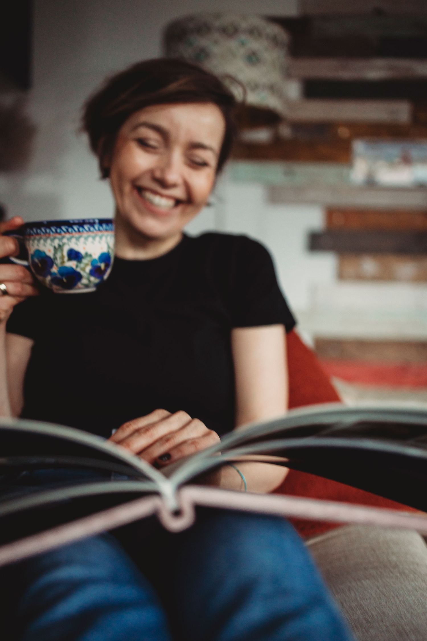 Person enjoying a quiet moment with a decorative blue teacup while reading a book on a comfortable couch.