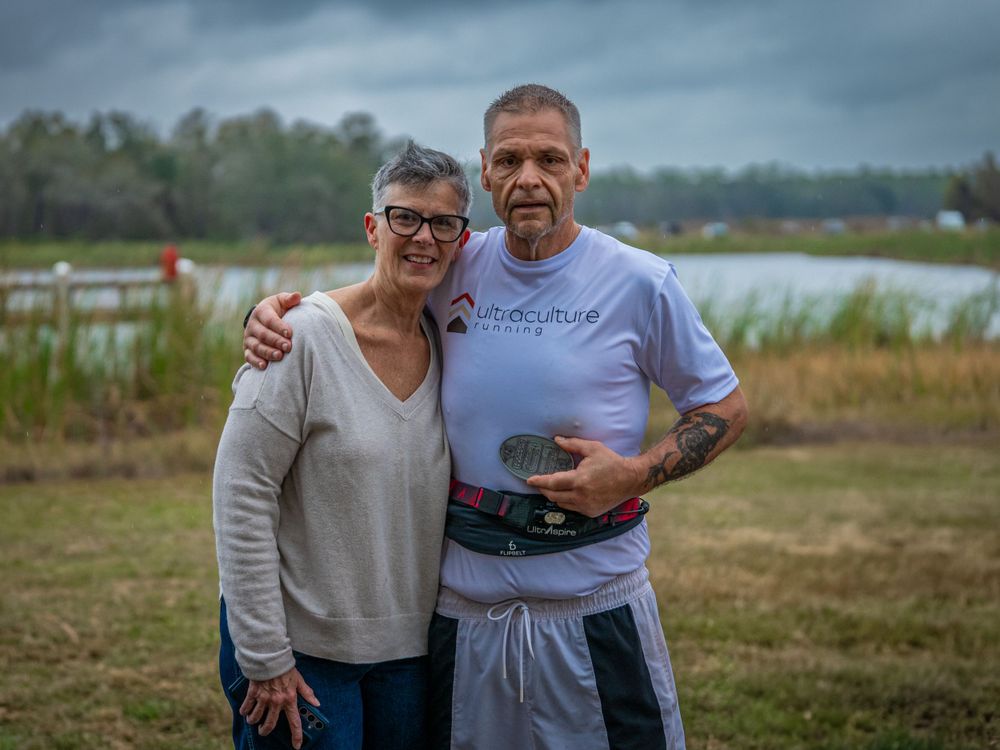 A couple poses together at an outdoor event with cloudy skies and water in the background.