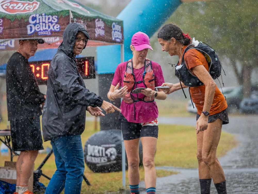 Group of runners checking devices while standing in the rain under a race banner.