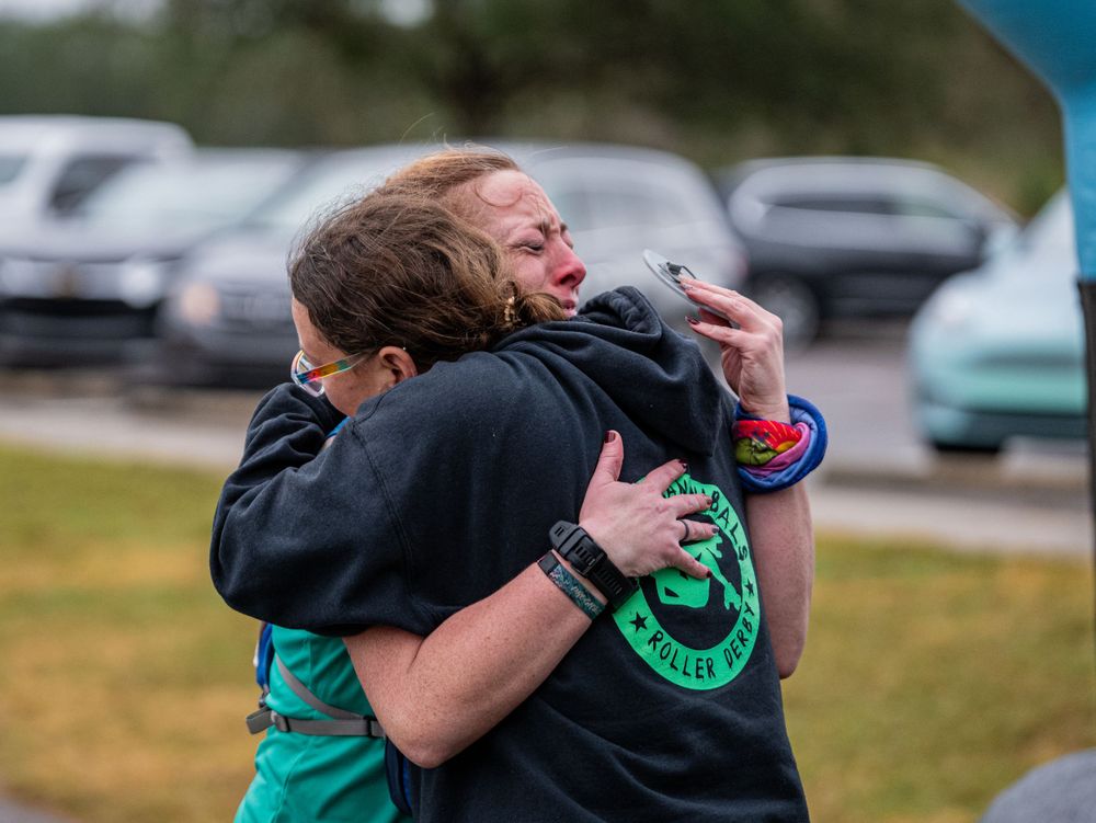 Two runners share emotional embrace at finish line of endurance race event.