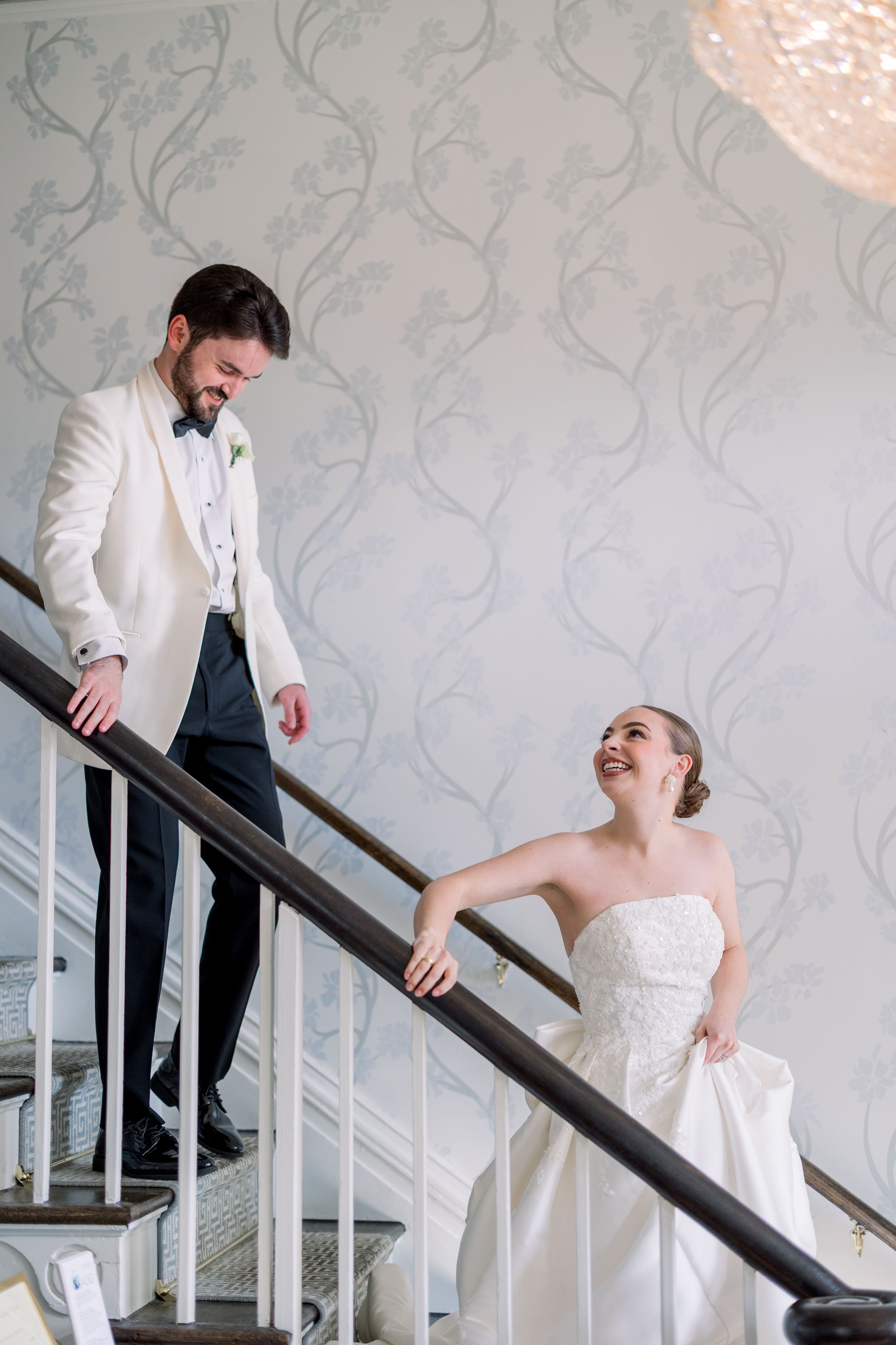 Elegant couple shares a moment on a staircase with floral wallpaper backdrop.
