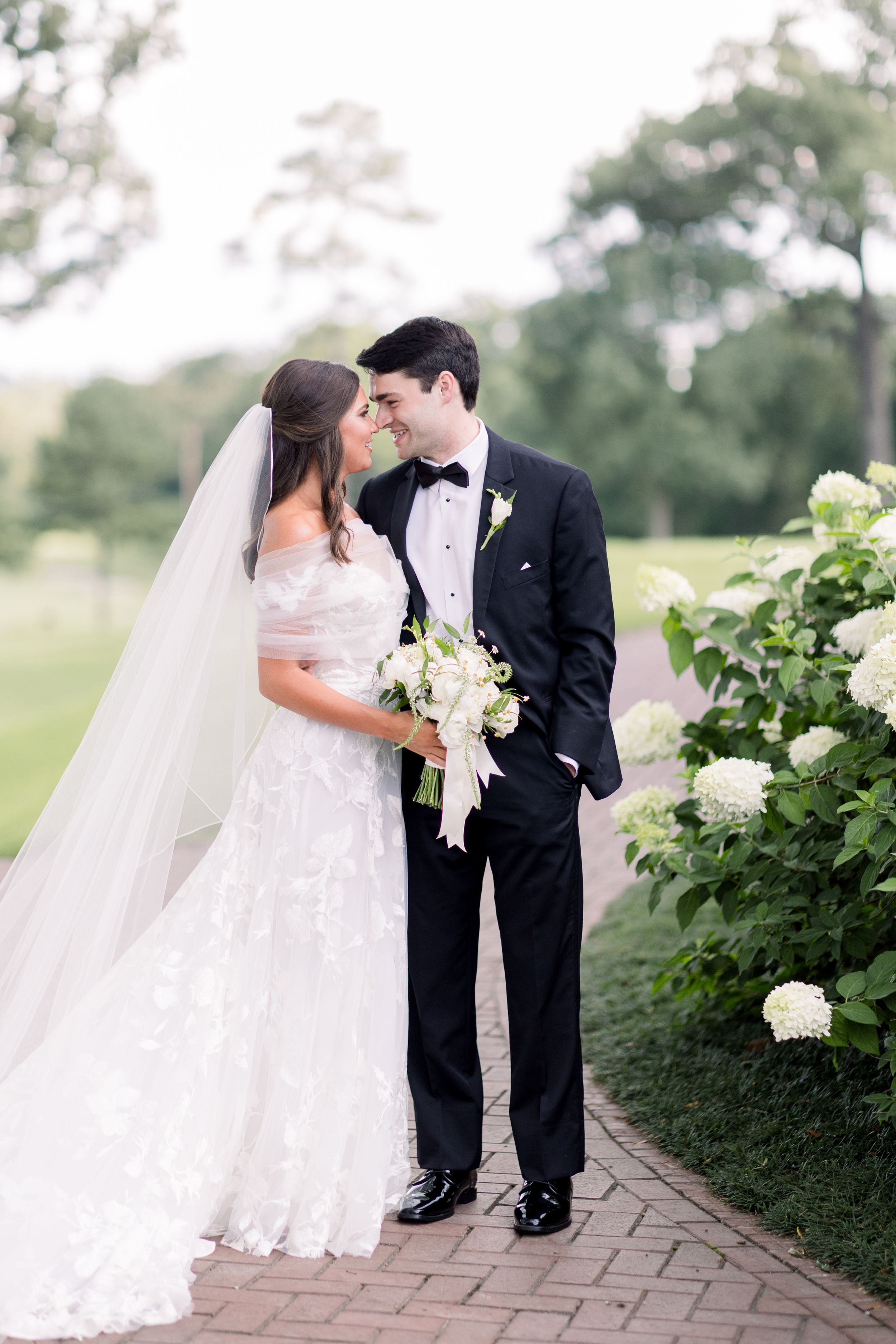 A romantic wedding couple shares intimate moments on a brick pathway surrounded by lush greenery.