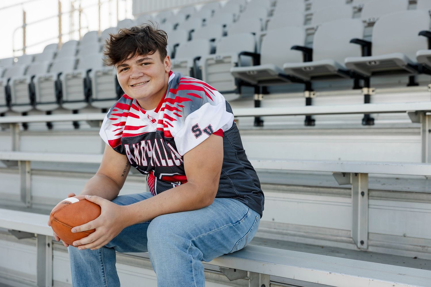 A person in a red and white striped shirt sits casually on bleachers at a sports stadium.