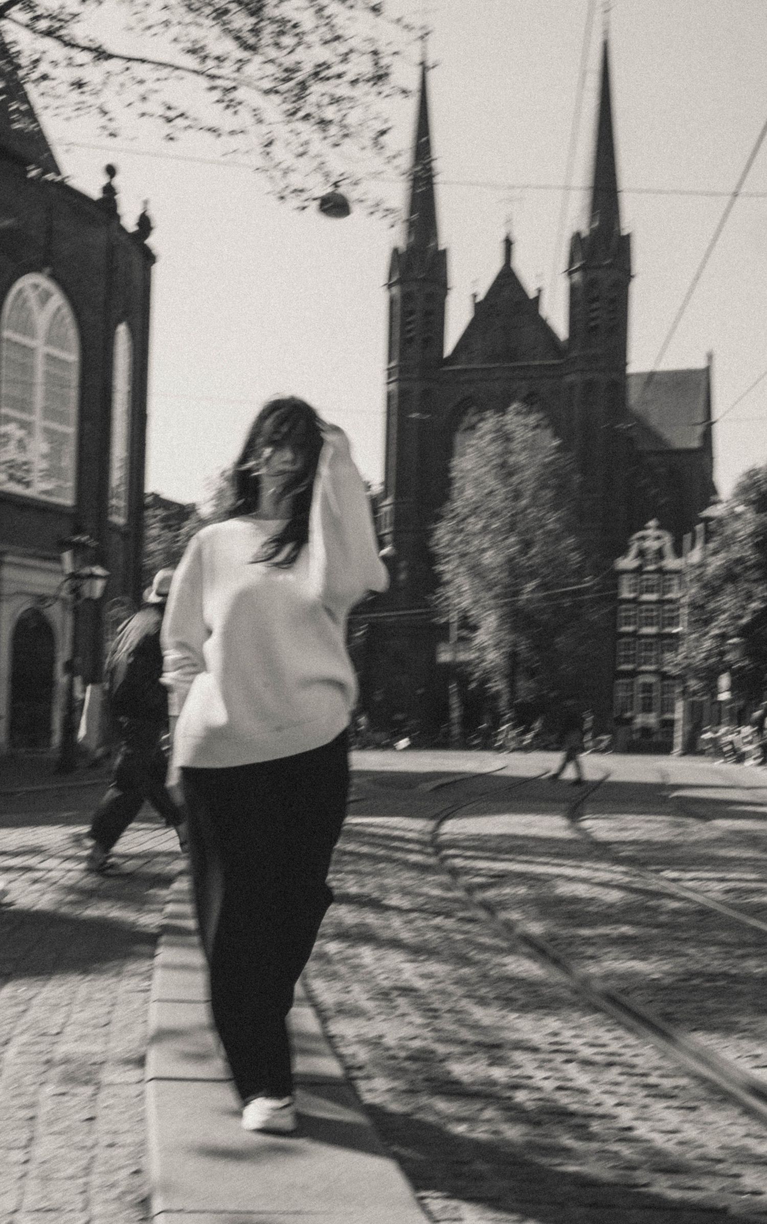 Cinematic motion photo—black and white analog-style portrait of a woman in an Amsterdam square with a church in the background.
