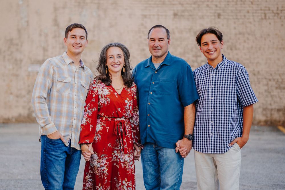 Family portrait session against a textured beige wall showing joyful expressions and coordinated casual outfits.