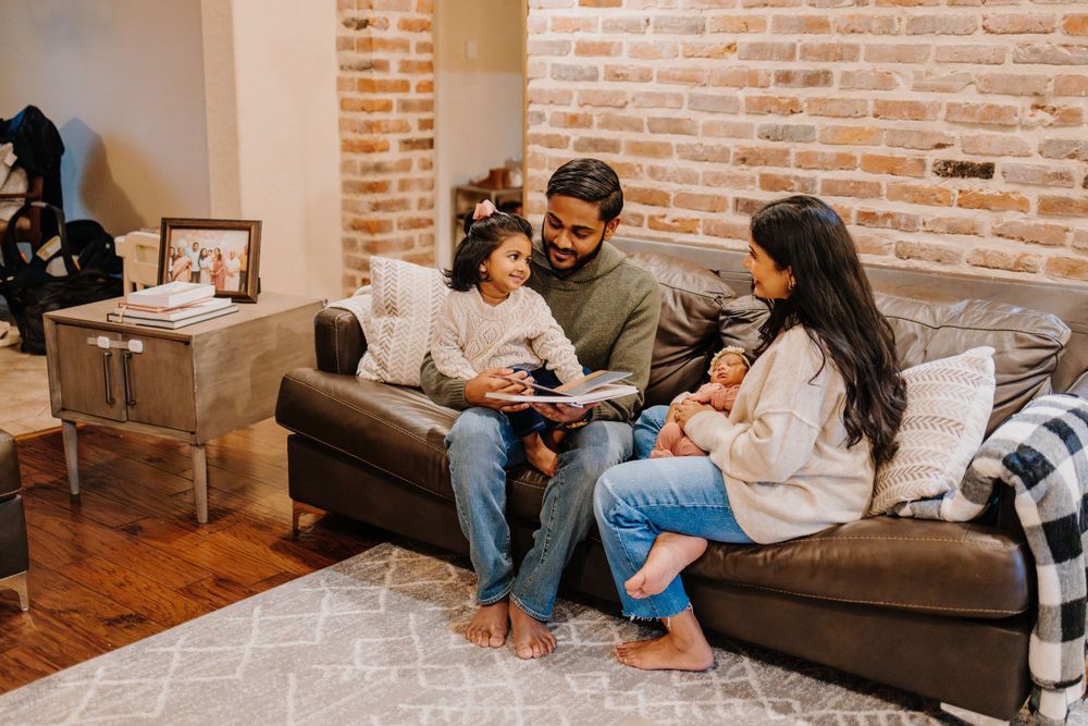 Family relaxing together on a brown leather couch in a brick-walled room.