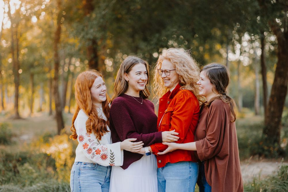 Four people wearing burgundy and red sweaters embrace while laughing together outdoors.