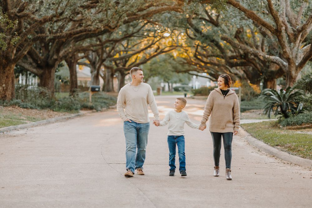 Family walking together on a tree-lined path during sunset creating long shadows.