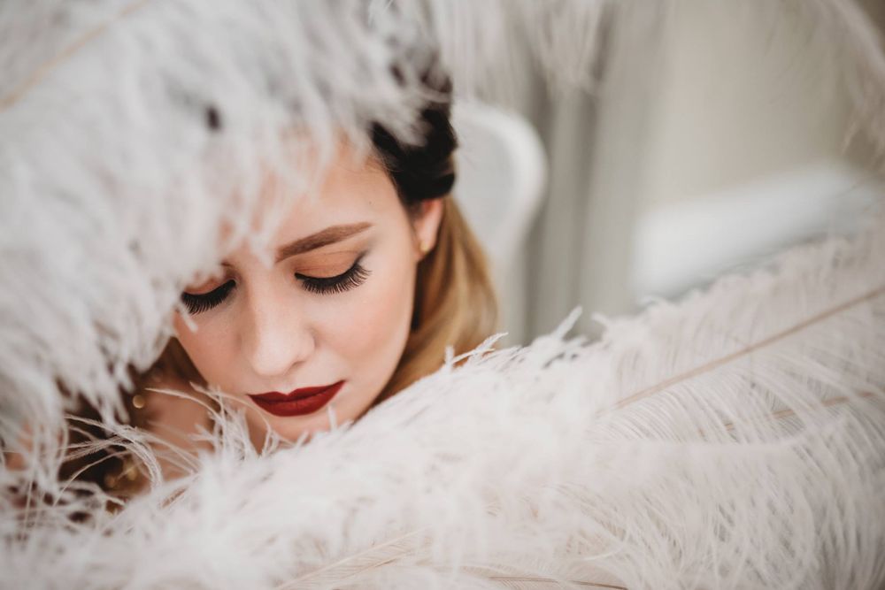Ethereal portrait series with white feathers and classic makeup styling.