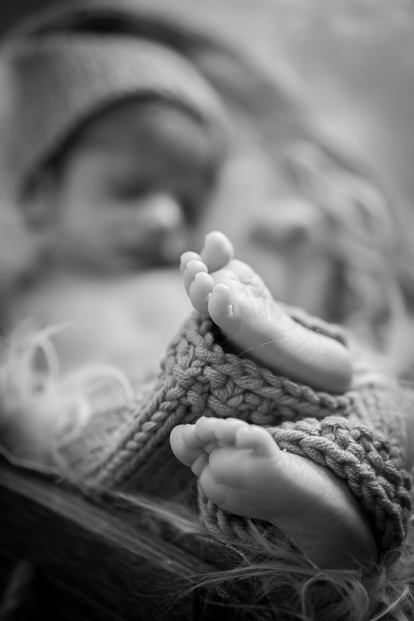 Close up black and white photo of tiny baby feet in knitted booties.
