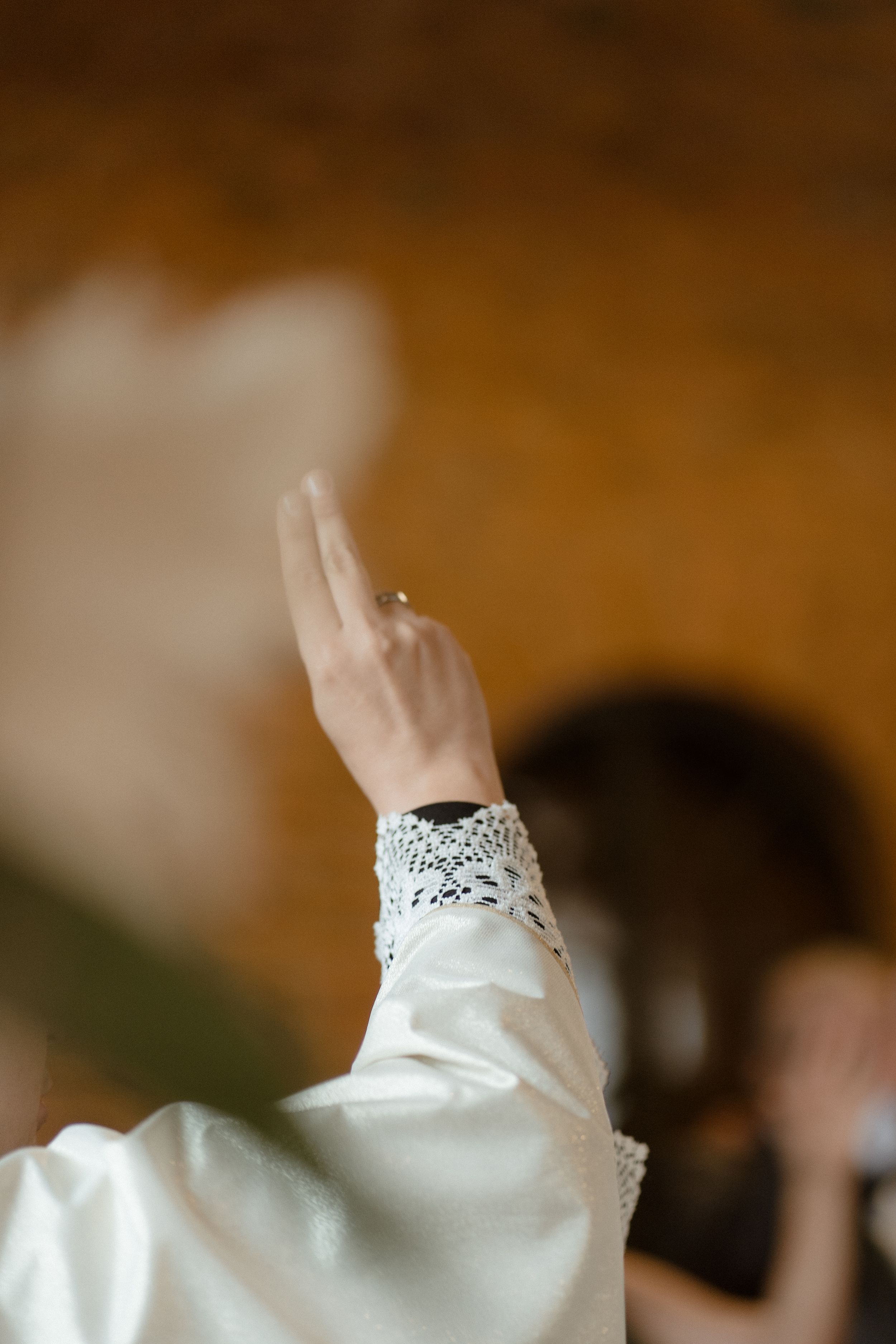 Close-up of lace detailed sleeve and raised hand during wedding ceremony.