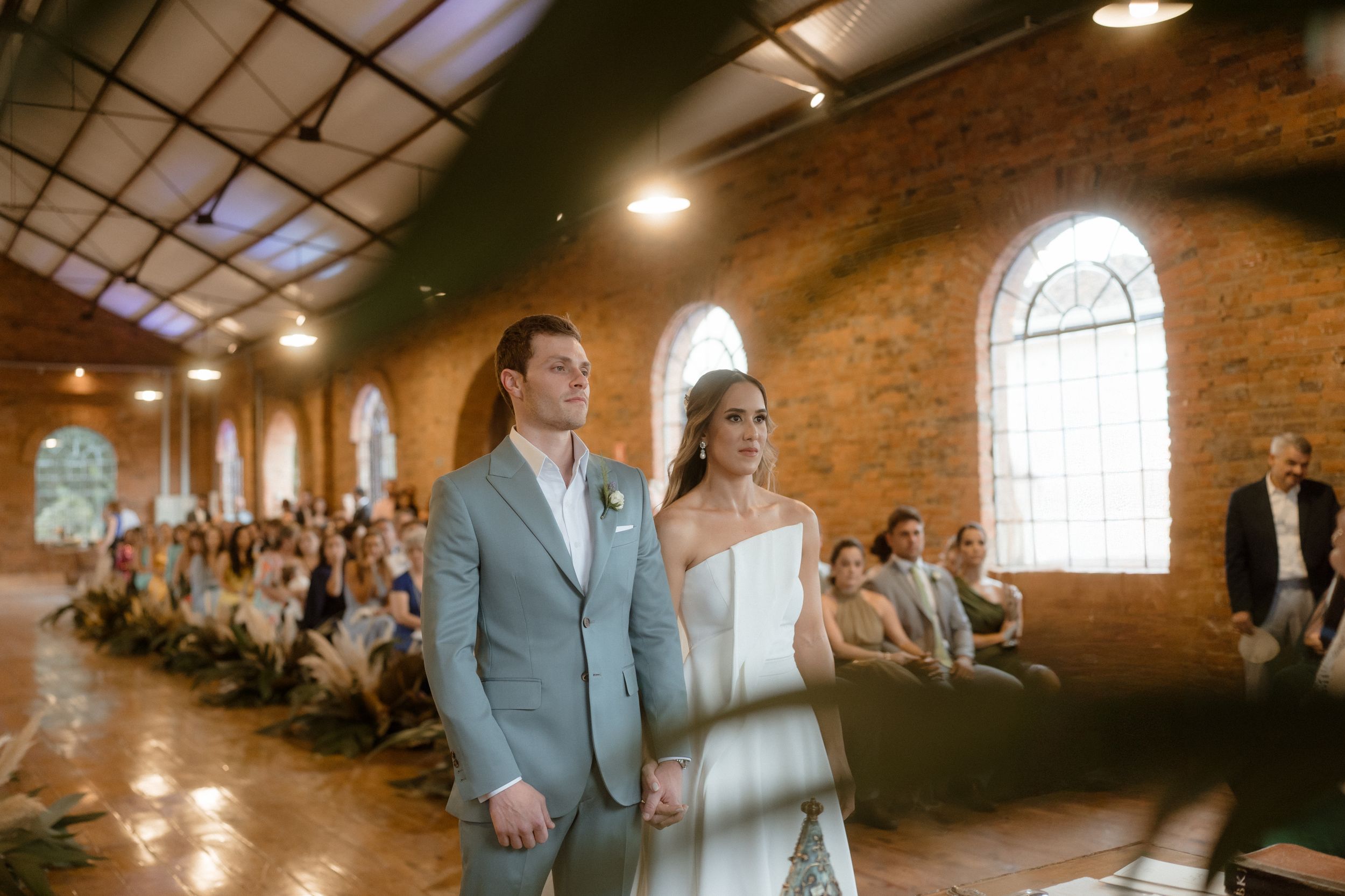 Wedding ceremony in historic brick venue with guests seated along the aisle watching the proceedings.