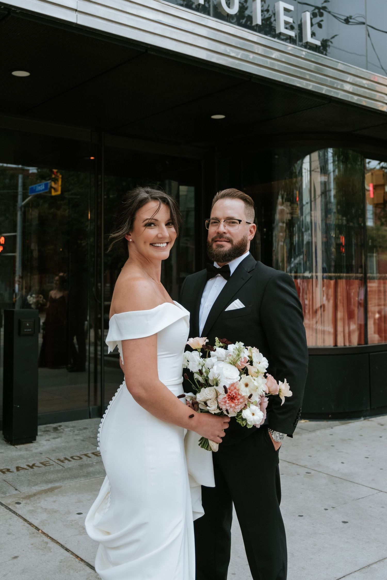 Wedding couple poses outside The Drake Hotel with elegant bouquet.