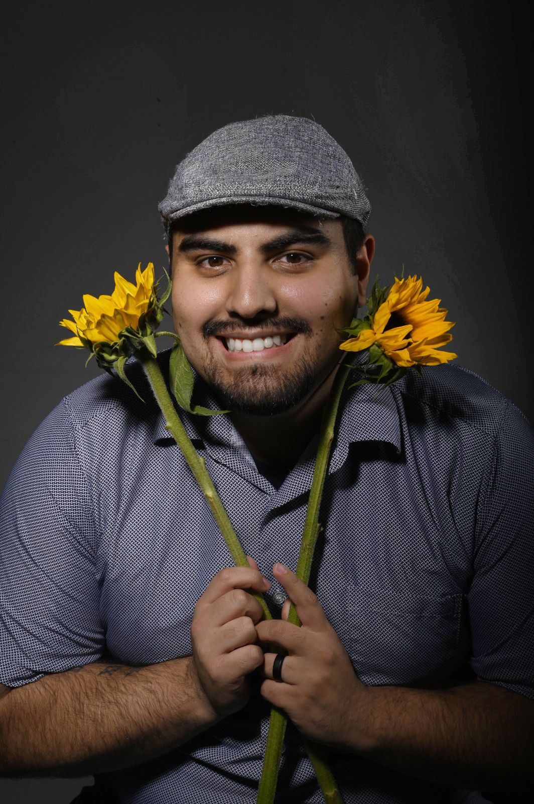 Portrait of the photographer in grey cap holding sunflowers with warm smile against dark background.