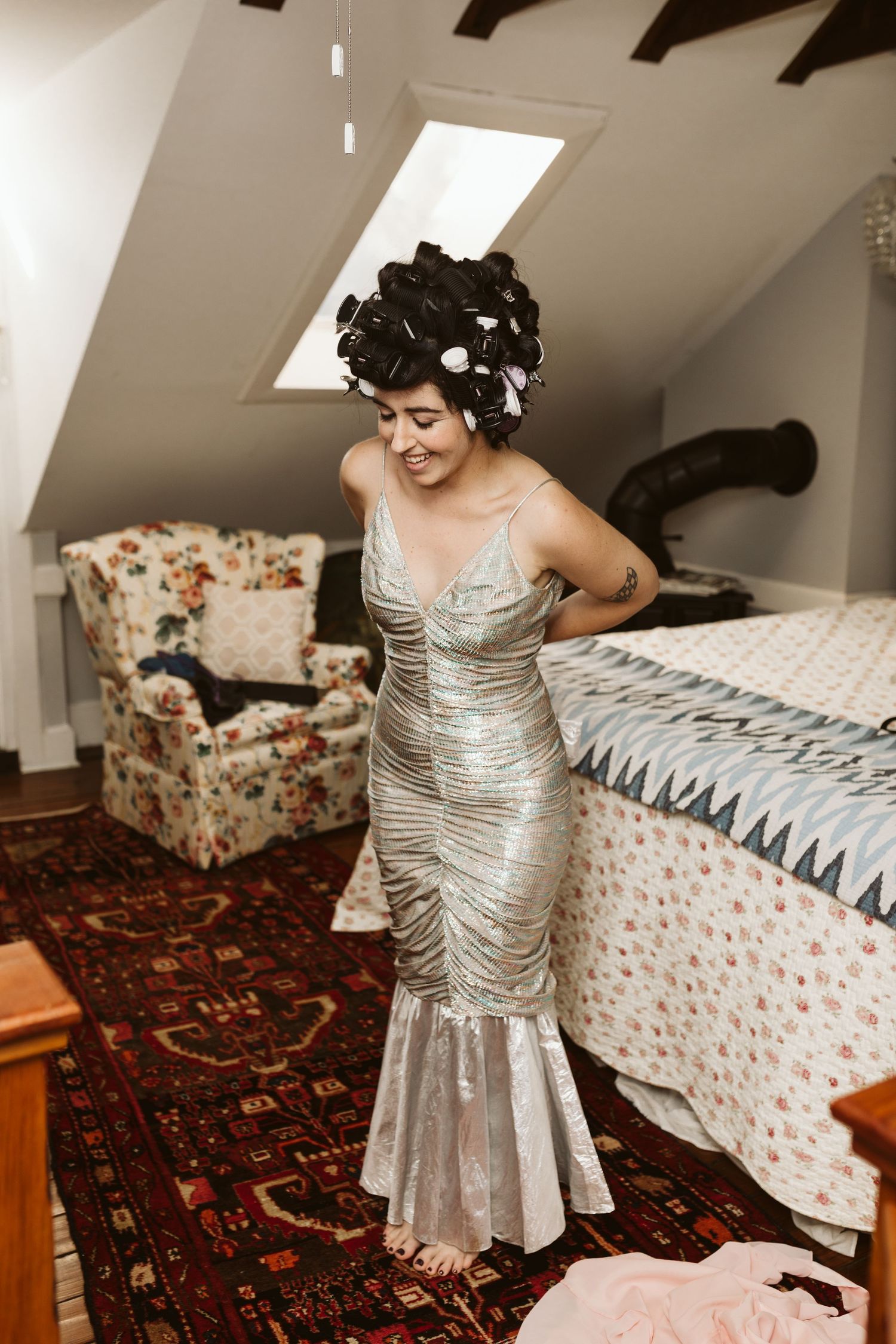 Person wearing a silver sequined dress twirls in front of a floral chair in a cozy attic room.