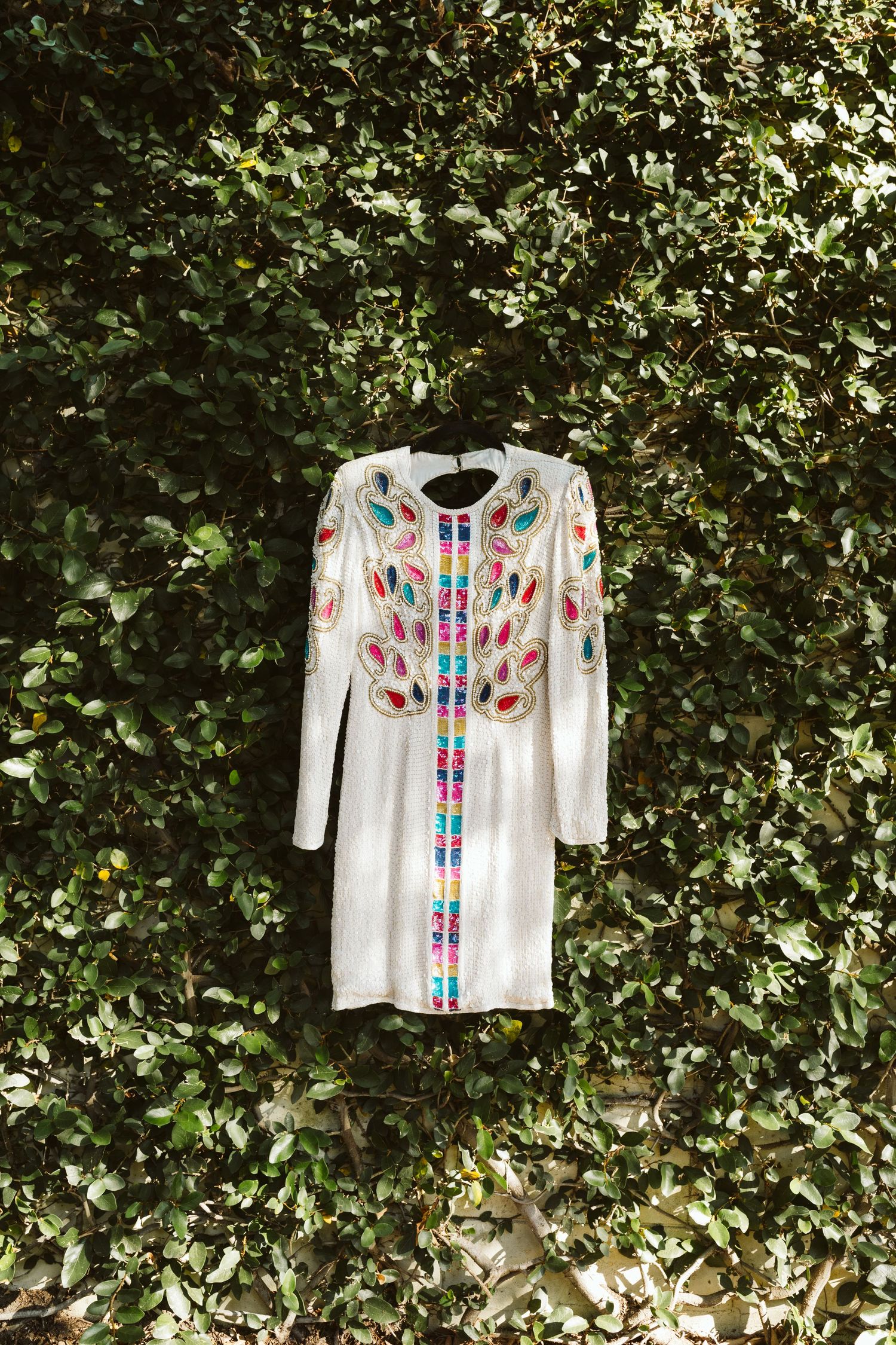 White embroidered top with colorful floral pattern hanging against green foliage.