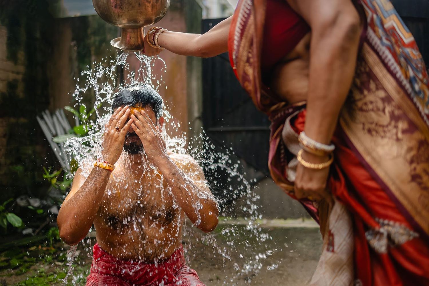 Water splashes on someone wearing traditional Indian clothing during a joyful ritual or celebration.