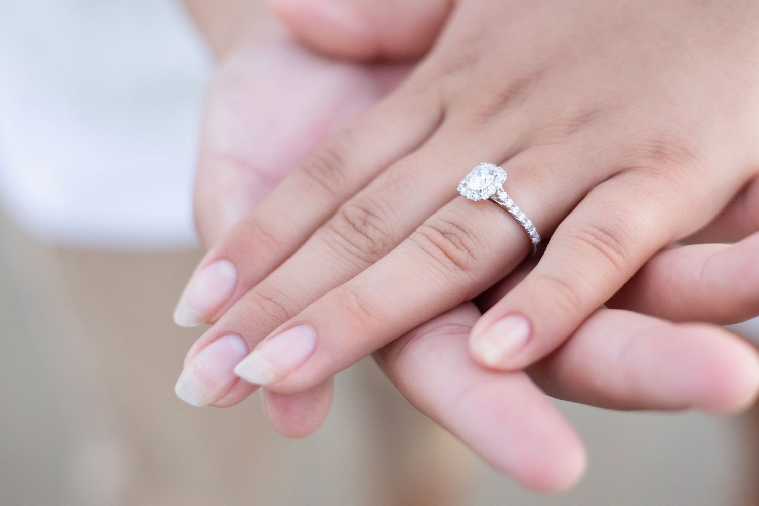 Close up of hands showing engagement ring with round solitaire diamond and delicate band.
