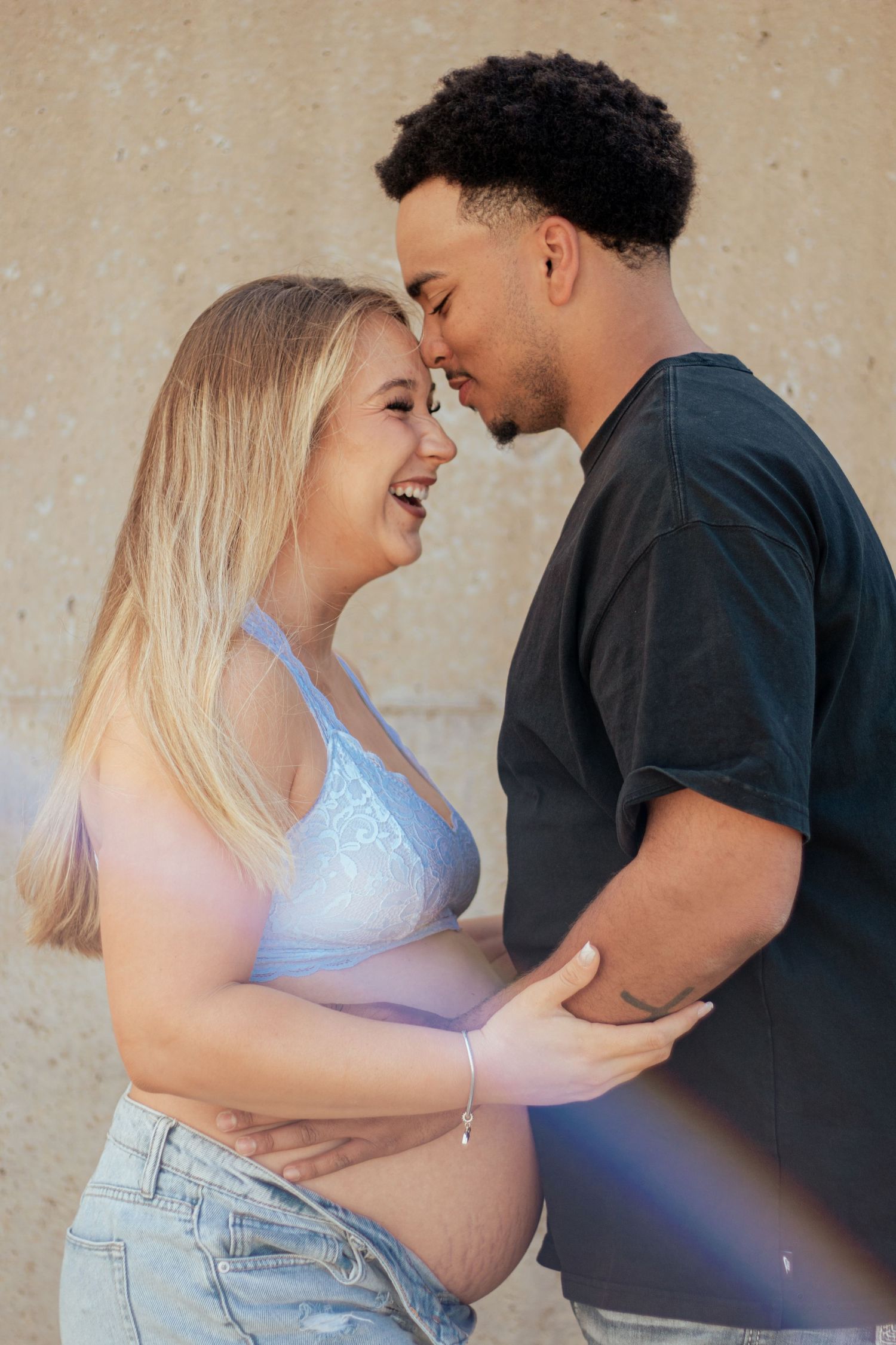 A tender maternity moment as an expecting couple shares a close embrace against a neutral wall background.