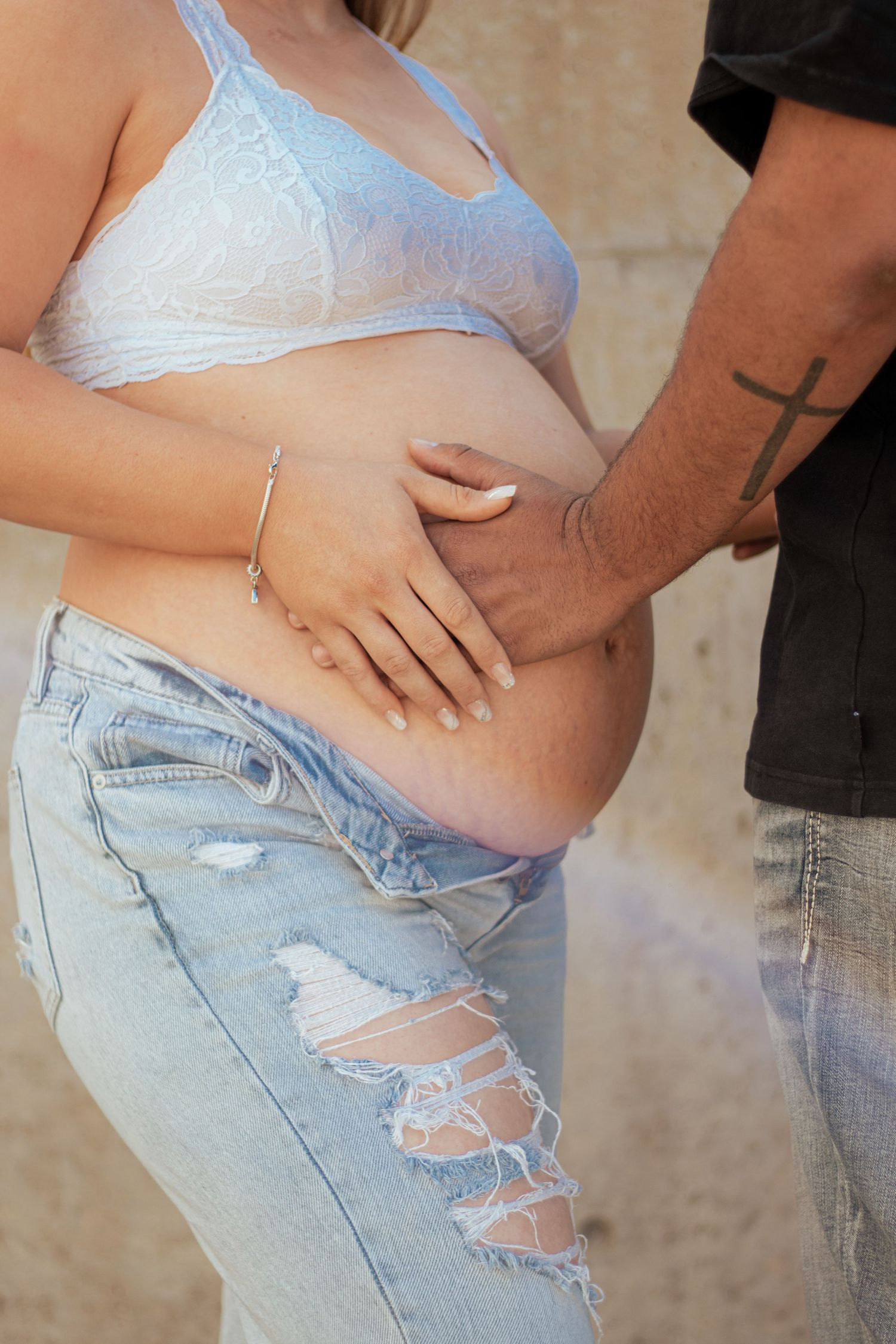 Close up of hands tenderly touching pregnant belly wearing ripped jeans and light blue bralette.