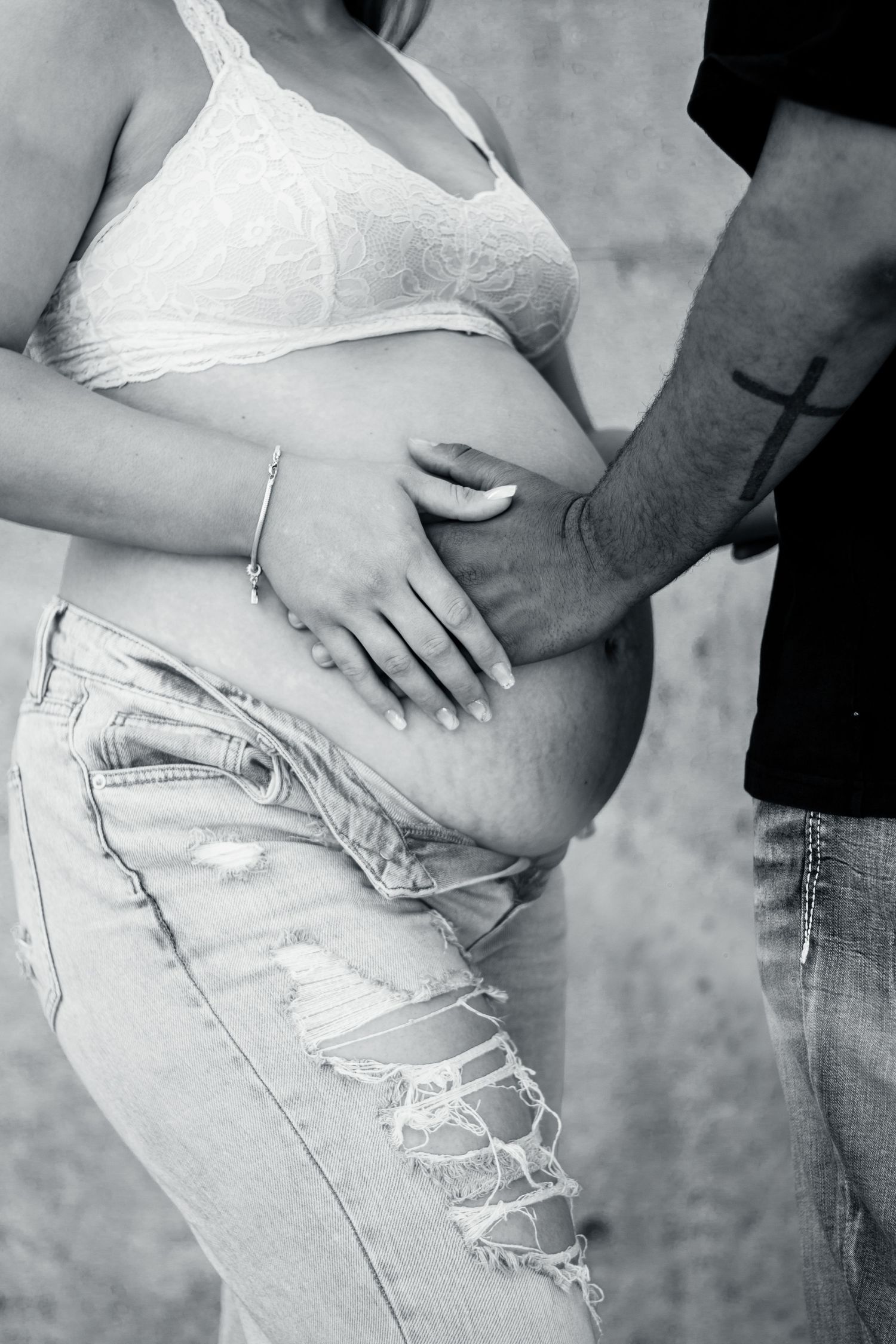Black and white maternity photo showing hands cradling a pregnant belly in distressed jeans and white top.