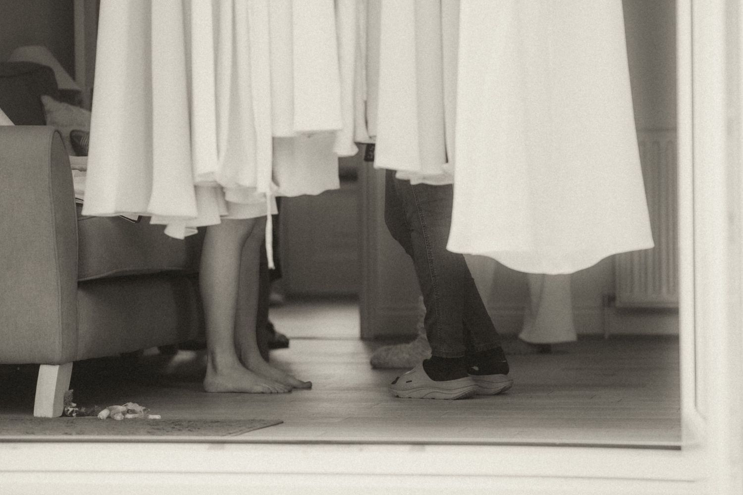A black and white photograph showing the lower body and feet of a person wearing dark clothing and standing behind a curtain.