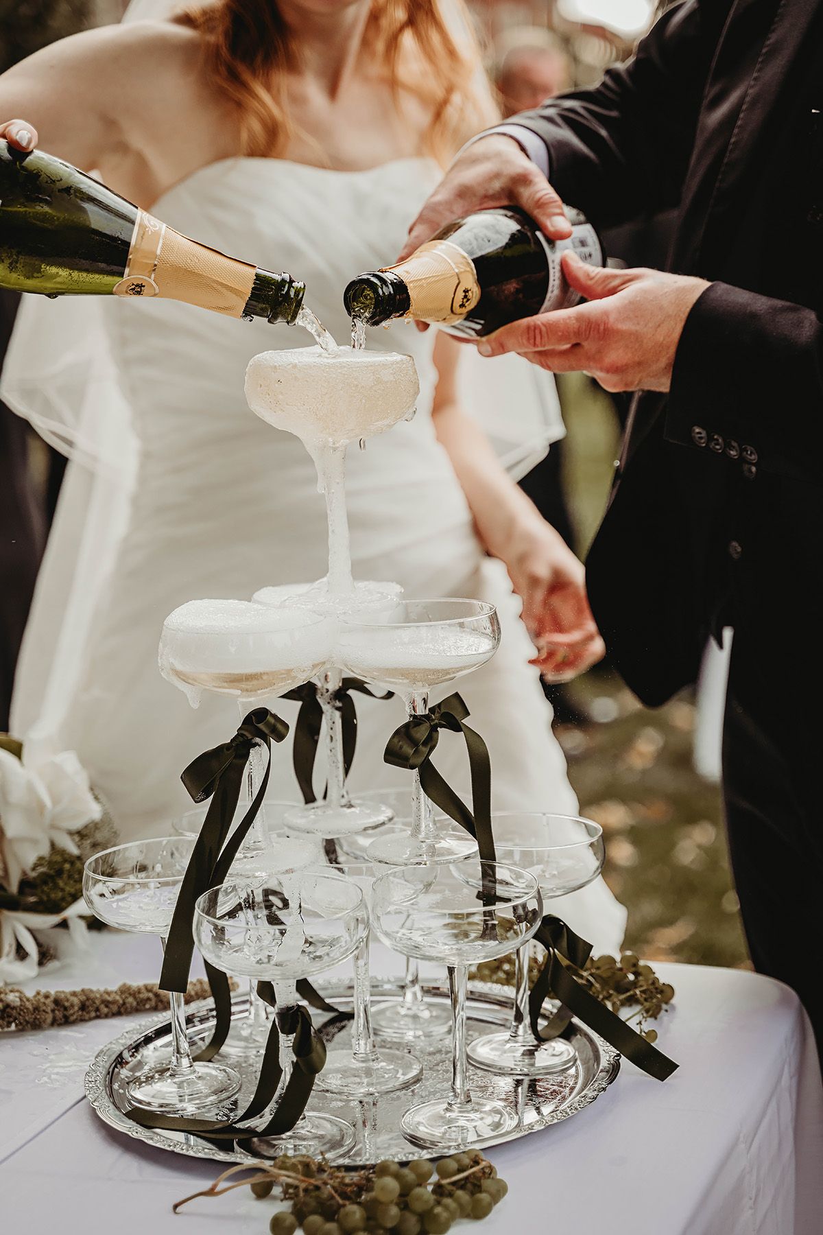 Champagnetorn på bröllop, brudpar häller upp champagne i ett vackert staplat torn av champagnekupor. Bröllopsfoto i Norrköping.