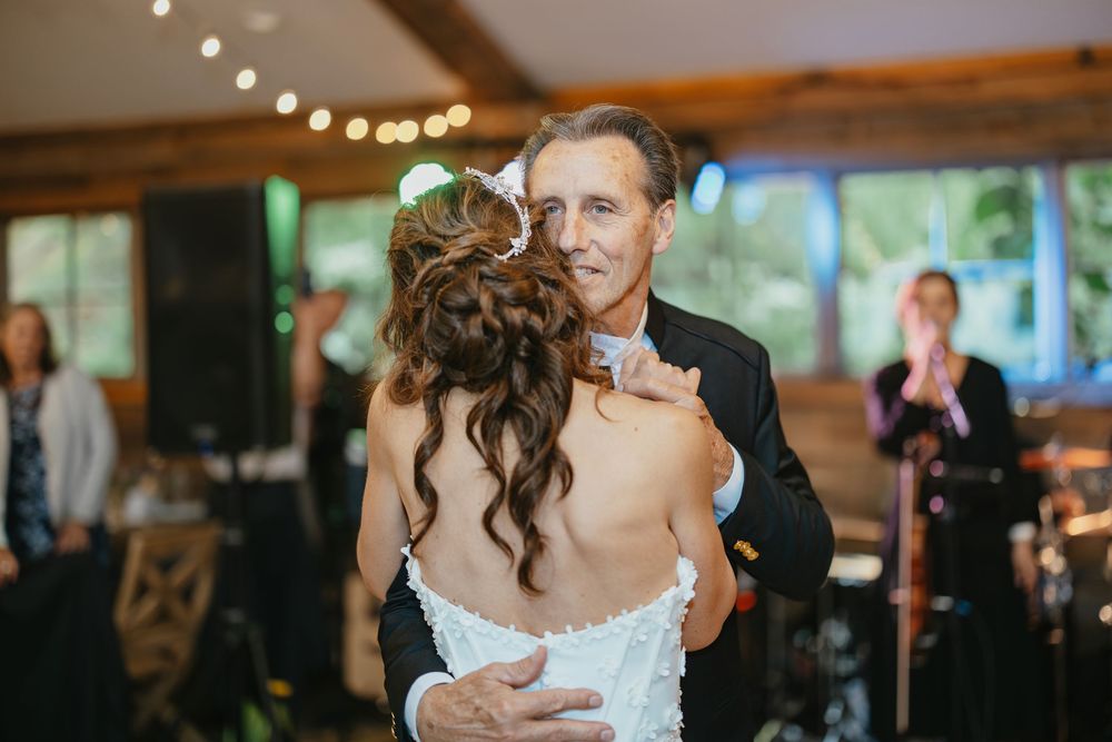 A romantic first dance moment at an elegant wedding reception with string lights and guests watching in the background.