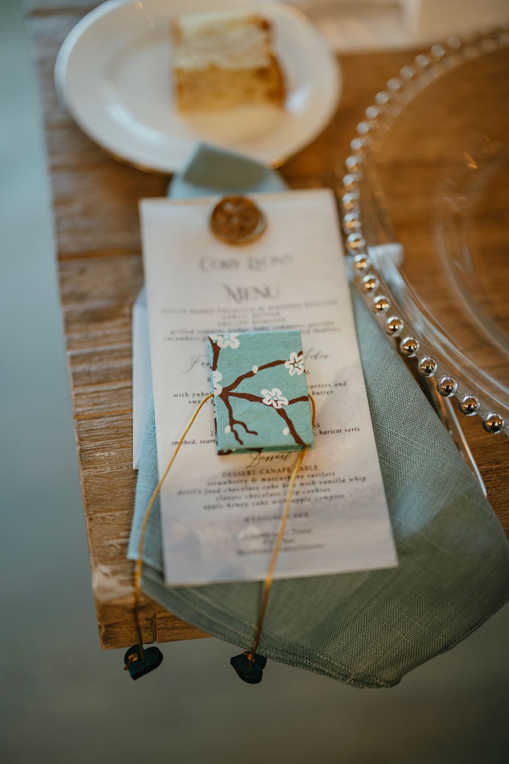 Wedding menu cards with sage green napkins and decorative twine displayed on rustic wooden table at reception.