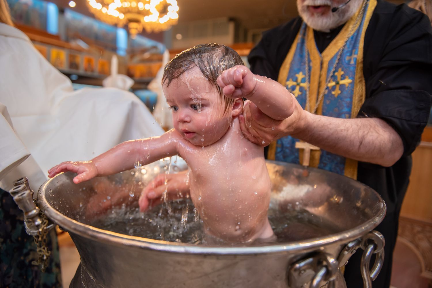 Infant being immersed in baptismal font by priest at St. Demetrios Greek Orthodox Church in Toronto