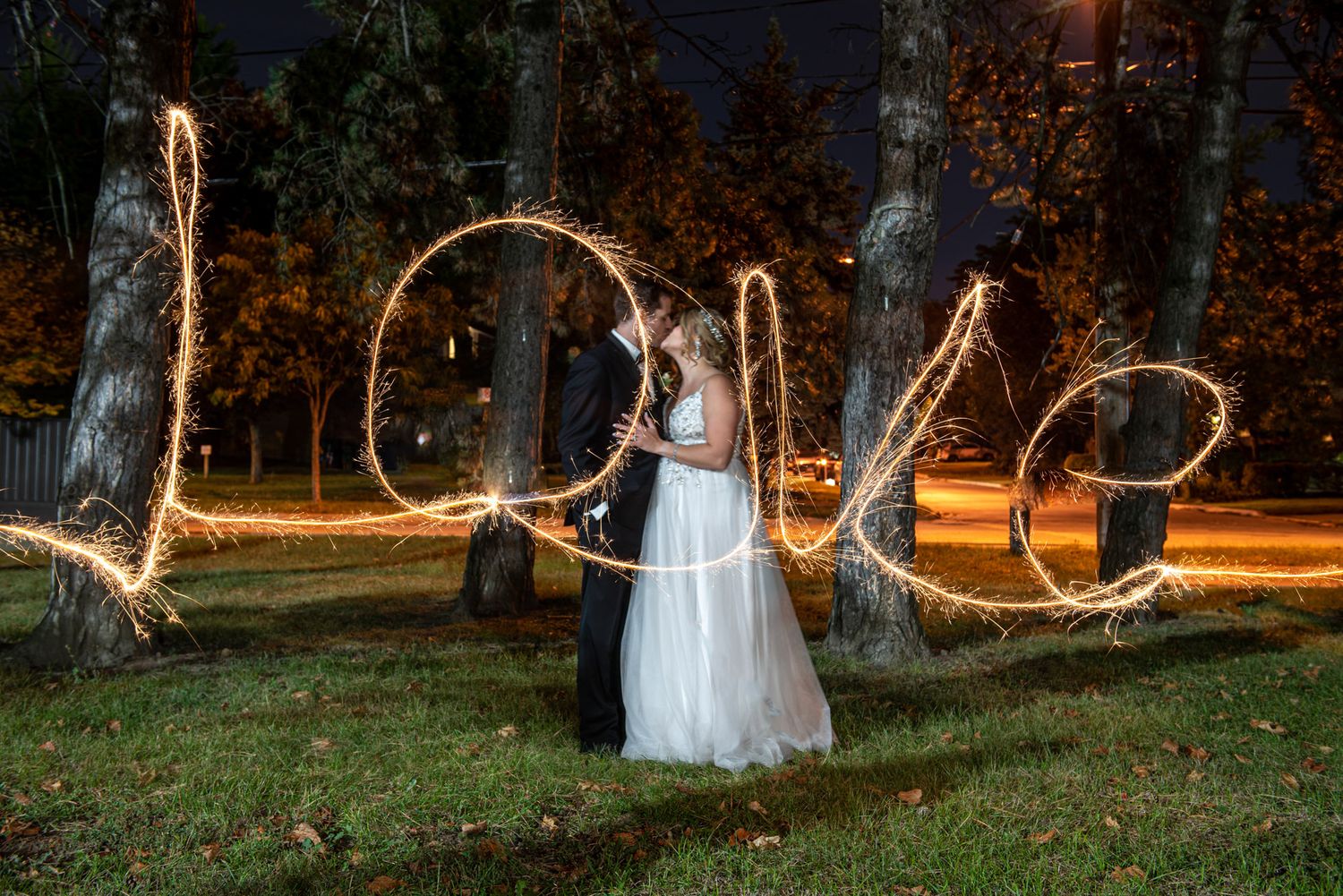 Bride and groom pose as sparklers spell Love in long exposure night wedding photo.